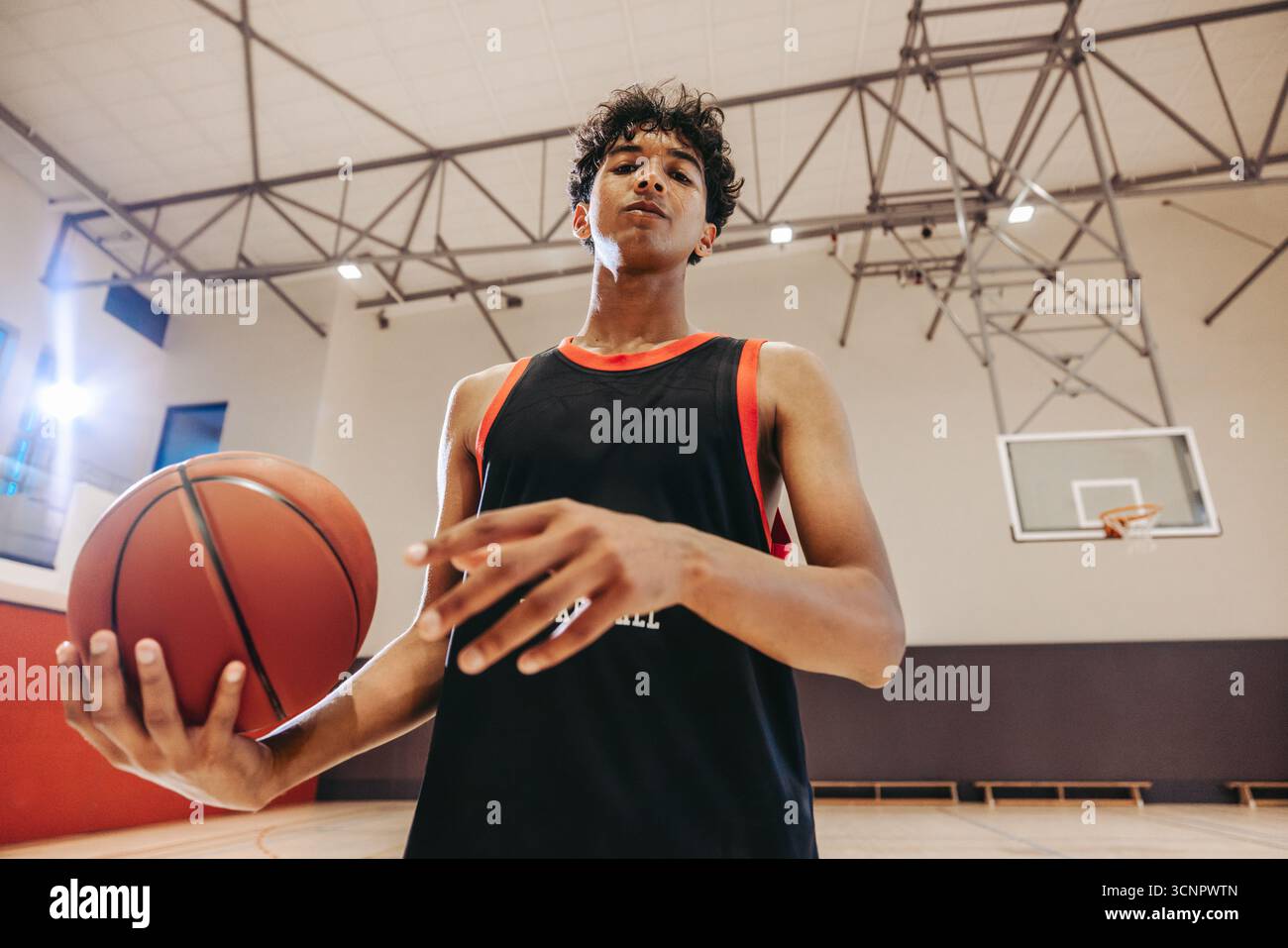 Giovane giocatore di basket maschile che gioca a pallacanestro in una palestra coperta, dimostrando determinazione, atletica e concentrazione in un ambiente sportivo. Foto Stock