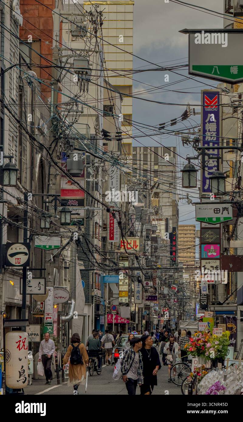 Vivace via di Osaka con linee elettriche aeree e insegne al neon Foto Stock