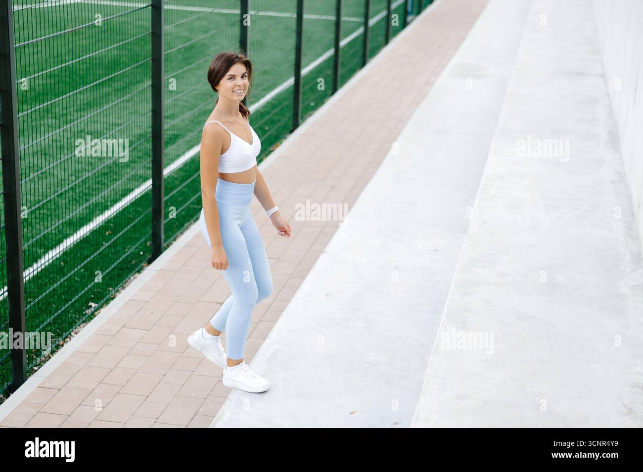 Fit Woman che si allena alle gambe con step-up in una struttura sportiva all'aperto, mostrando dedizione e forza in un ambiente estivo vivace Foto Stock