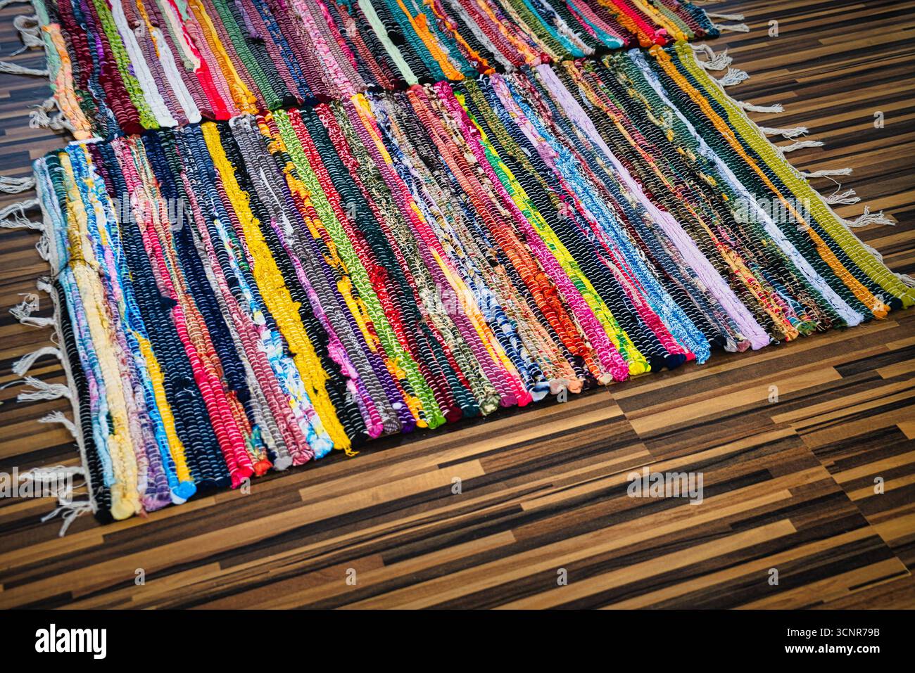 Vivaci tappeti in tessuto a mano multicolore disposti su pavimento in parquet scuro in un accogliente ambiente interno Foto Stock
