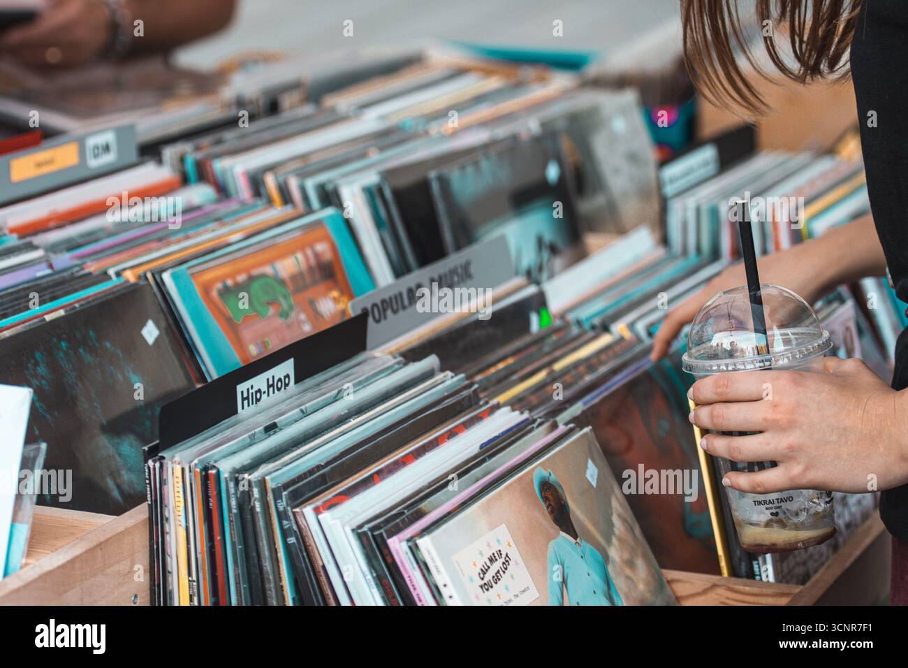 Ragazza che sfoglia dischi in vinile in casse di legno in un negozio di musica o al mercato delle pulci. Primo piano di mani che sfogliano album LP vintage Foto Stock