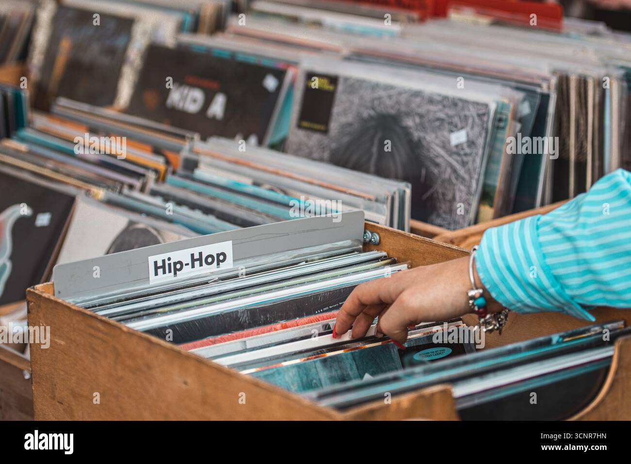 Ragazza che sfoglia dischi in vinile in casse di legno in un negozio di musica o al mercato delle pulci. Primo piano di mani che sfogliano album LP vintage Foto Stock