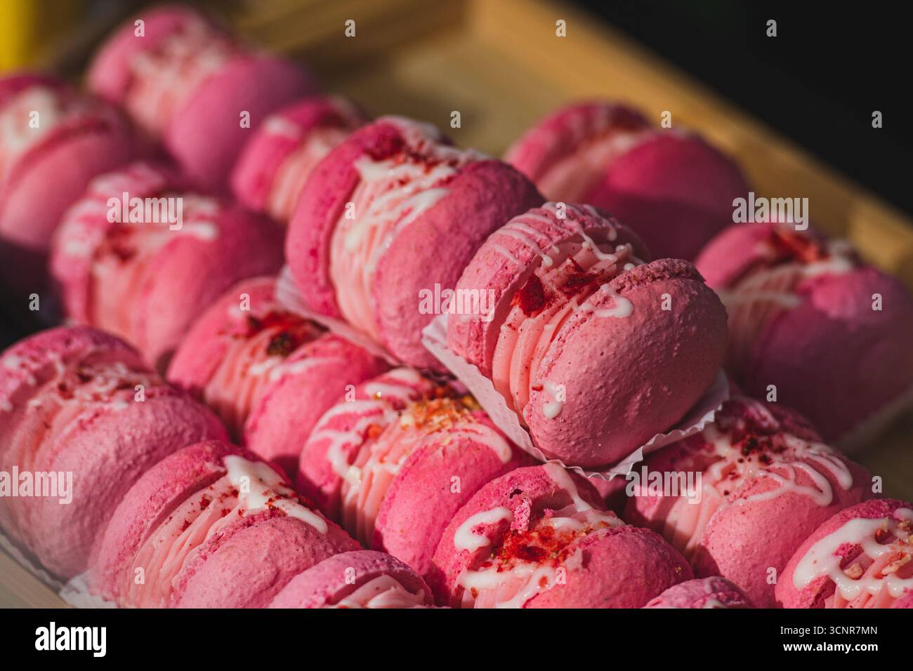 Primo piano di macaron rosa disposti in righe. Dolce dolce francese con ripieno di panna, decorato con glassa bianca e briciole. Colorato e discreto Foto Stock