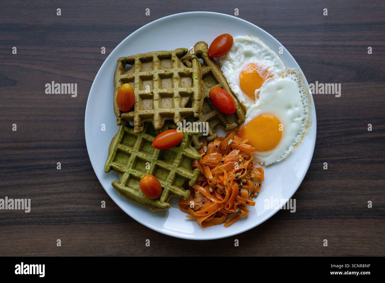 Vista dall'alto del piatto salutare della colazione con waffle verdi, uova fritte e verdure su un tavolo di legno, concetto di brunch, nutrizione. Foto Stock