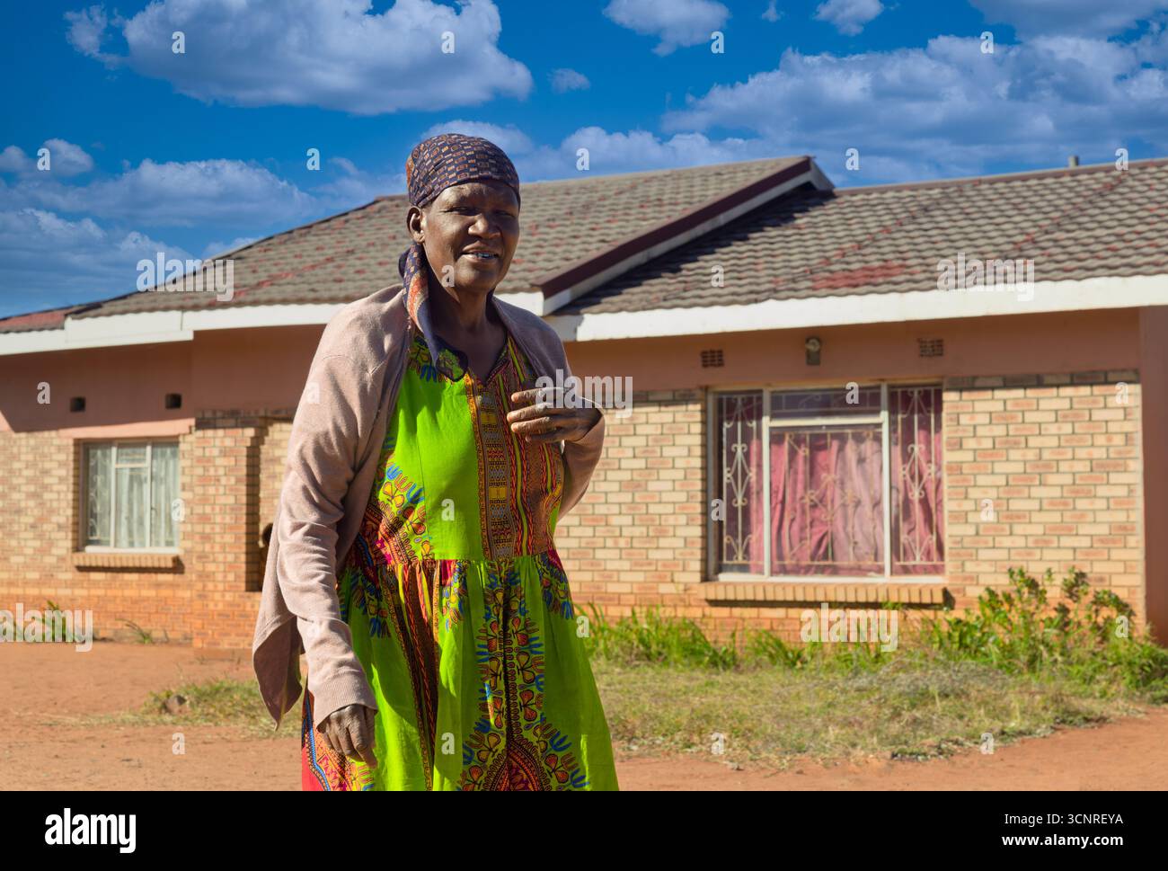 africa village, copricapo per donna anziana africana nella cittadina, look duro, in piedi all'aperto nel cortile di fronte alla porta della casa Foto Stock