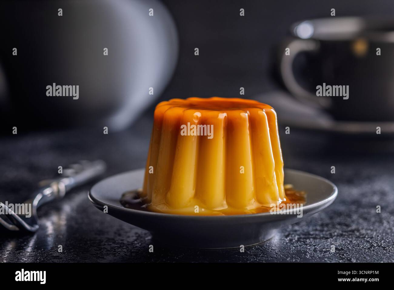 Budino alla vaniglia con salsa al caramello su un tavolo nero. Foto Stock