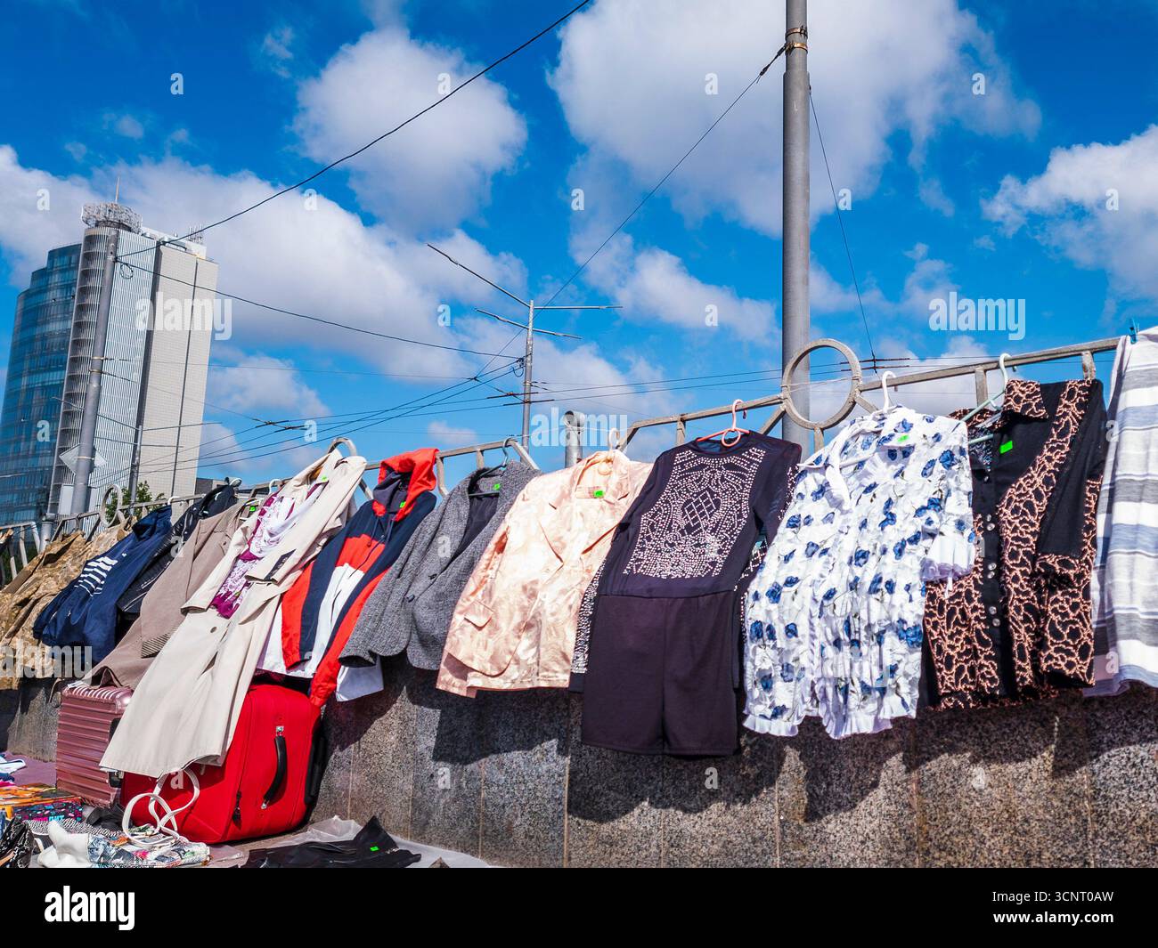 Kiev, Ucraina 10 maggio 2025, mercato delle pulci all'aperto a Kiev con abiti appesi contro il cielo azzurro, edifici cittadini e linee elettriche, che mostrano la cultura urbana di strada e la moda di seconda mano Foto Stock