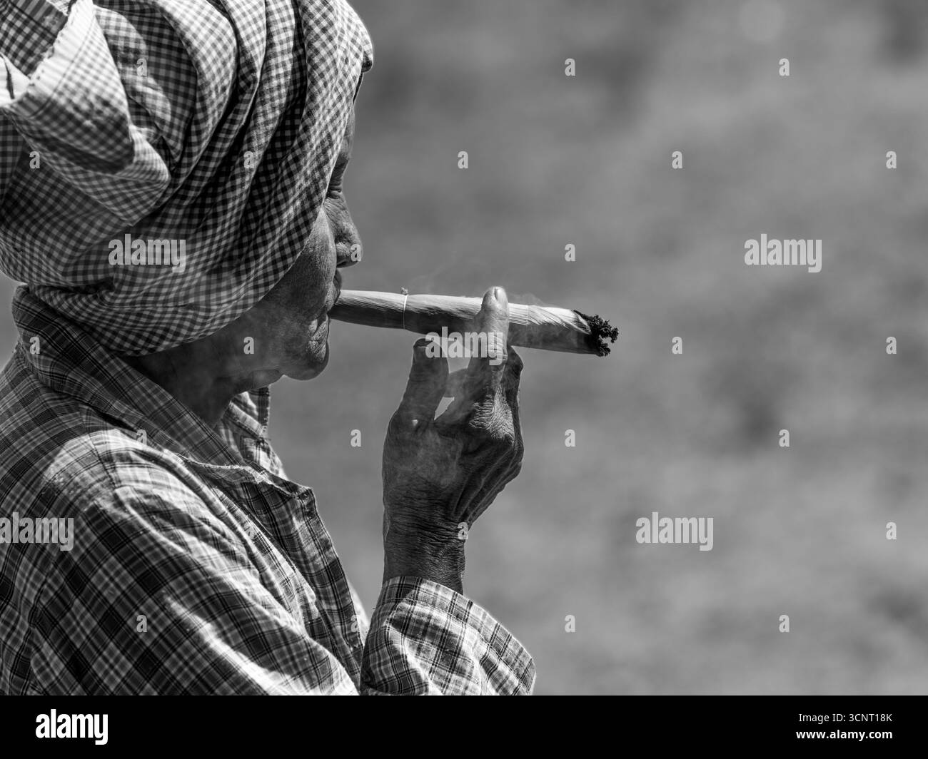 Donna anziana che fuma sigaro tradizionale in bianco e nero - Ritratto culturale con rughe, velo e stile di vita rurale Foto Stock