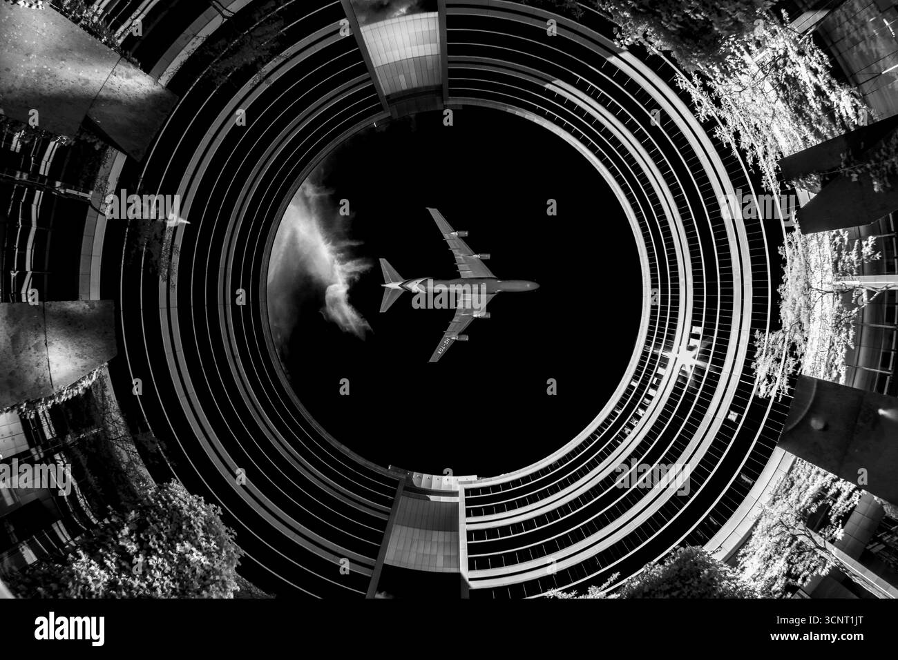 Aereo che vola di notte incorniciato da un'architettura circolare moderna in una spettacolare prospettiva in bianco e nero con simmetria surreale Foto Stock