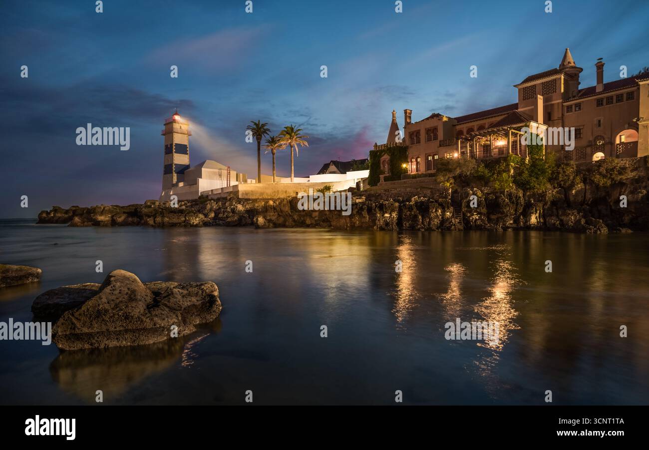 Faro panoramico di notte con architettura costiera illuminata, palme e riflessi nelle calme acque oceaniche del Portogallo Foto Stock