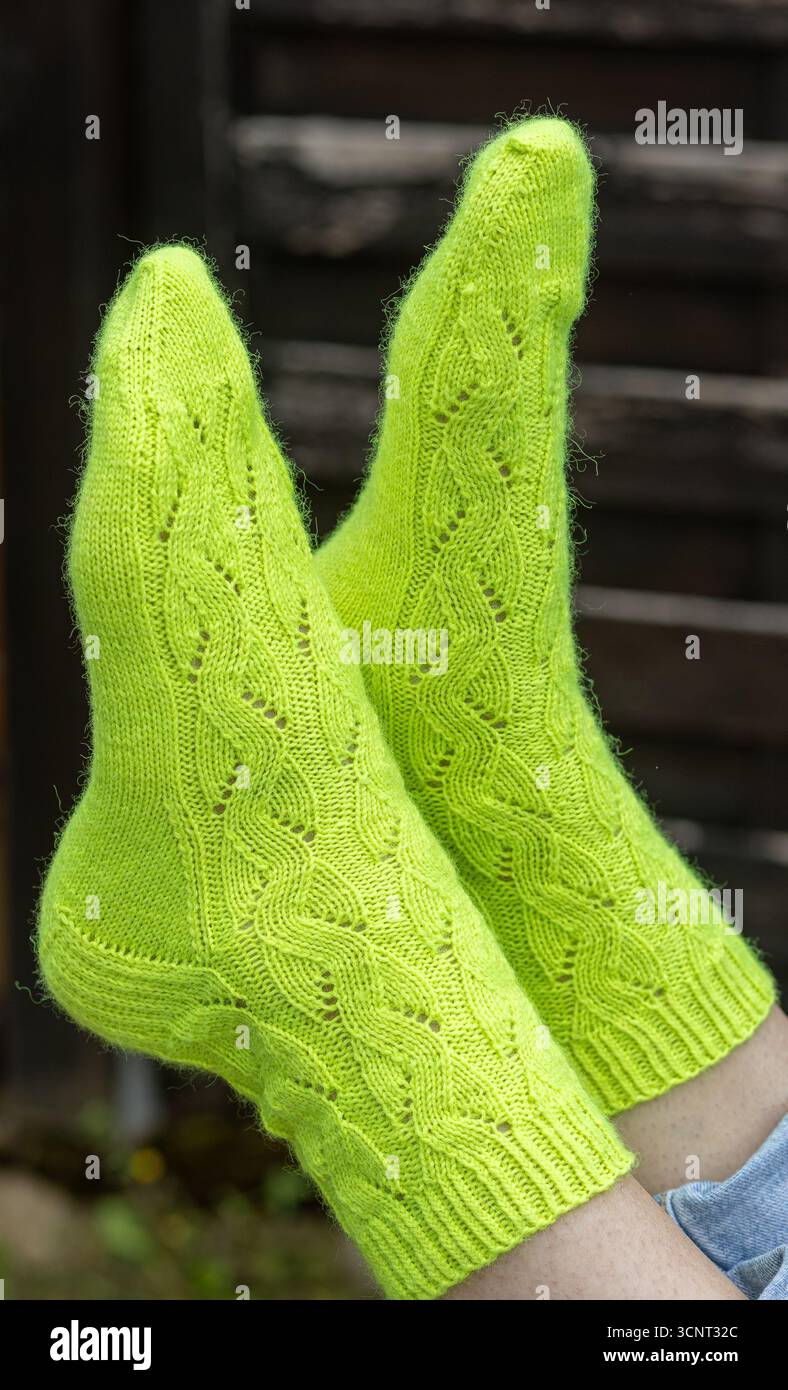 Un paio di calzini verdi vivaci con un design a maglia di cavi. La scena offre un'atmosfera accogliente, perfetta per un pomeriggio rilassante a casa, sur Foto Stock