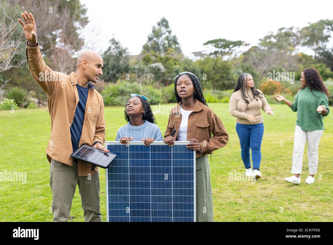 Famiglia diversificata che dimostra l'energia solare tenendo piccoli e grandi pannelli solari su prato verde Foto Stock