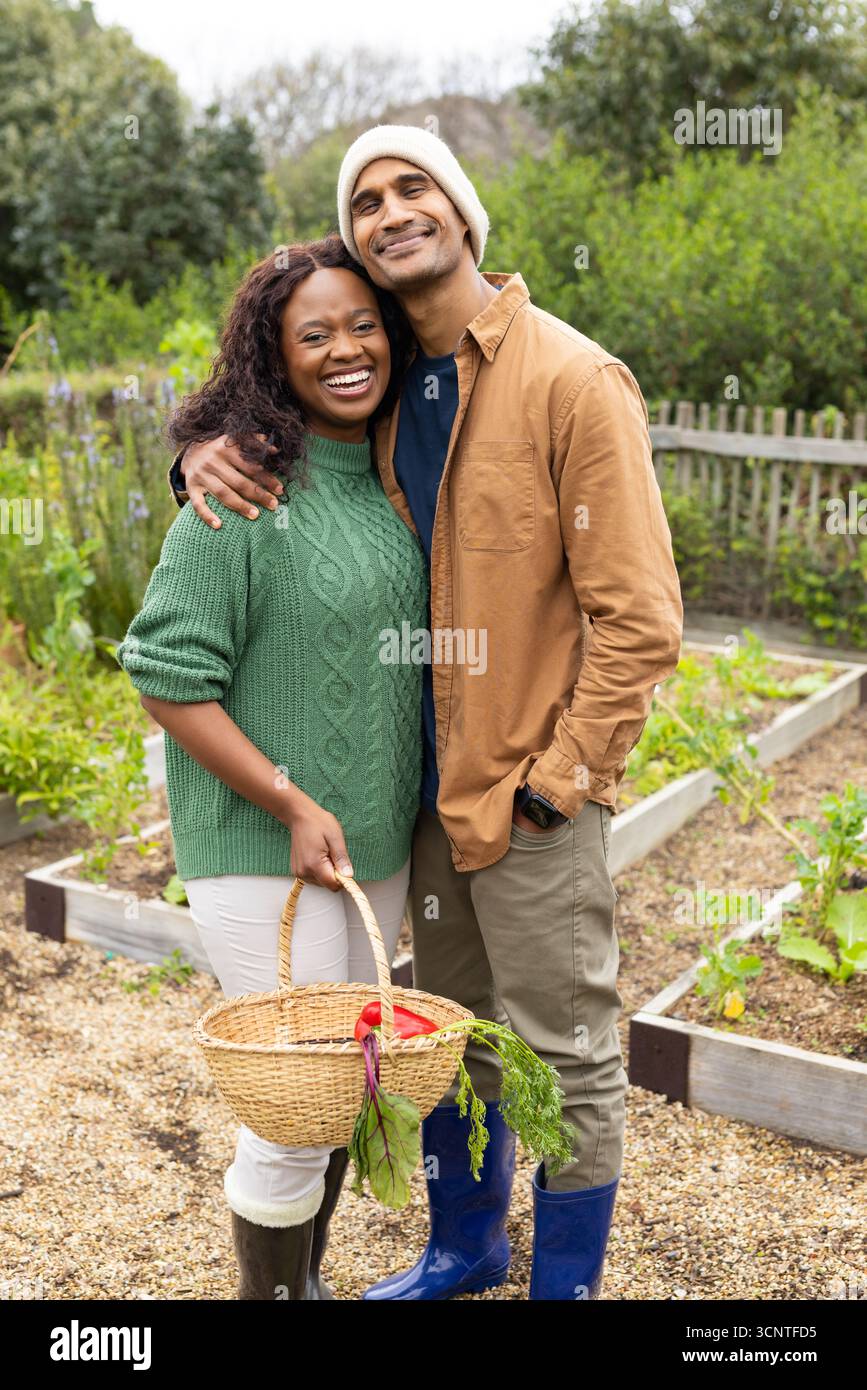 Diverse coppie in piedi tra letti rialzati che tengono un cesto di vimini pieno di barbabietole nel giardino di casa Foto Stock