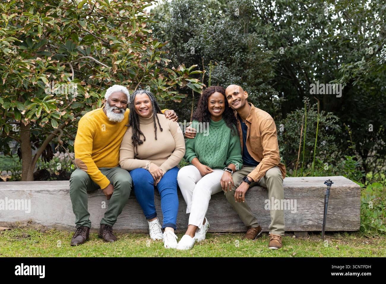 Famiglie diverse sedute su una panchina di legno in giardino e inclinate verso il treppiede della fotocamera Foto Stock
