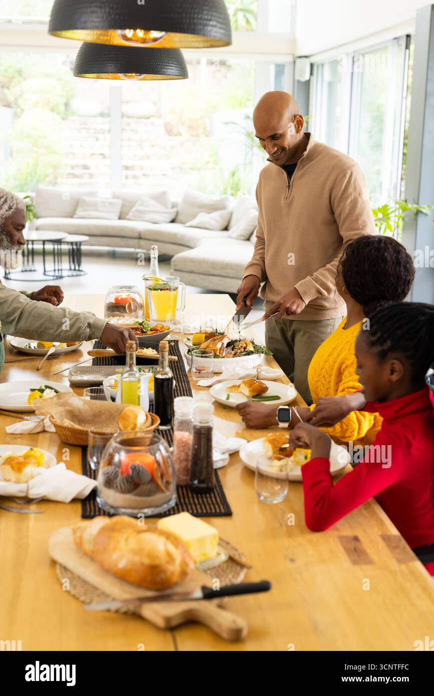 Diversi pasti per famiglie attorno a un tavolo di legno nella zona pranzo, con piatti di carne arrosto Foto Stock