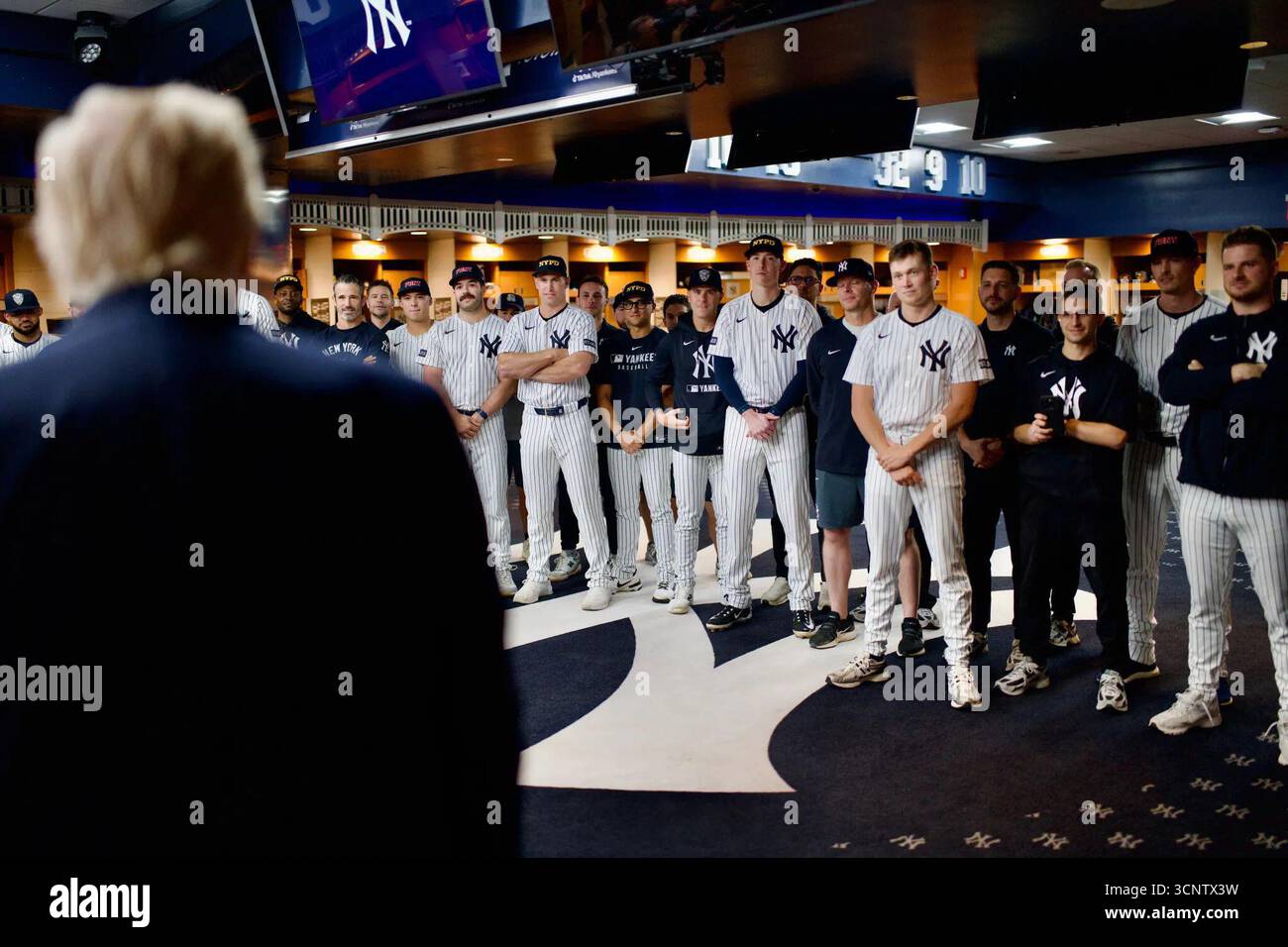 Il presidente Donald Trump parla con la squadra dei New York Yankees nel loro spogliatoio della clubhouse indossando per la NYPD e la FDNY cappelli tributo per il 9/11 prima di una partita contro i Detroit Tigers allo Yankee Stadium. I giocatori ascoltano in uniforme da pinstripe. New York, Stati Uniti. 11 settembre 2025. Foto Stock