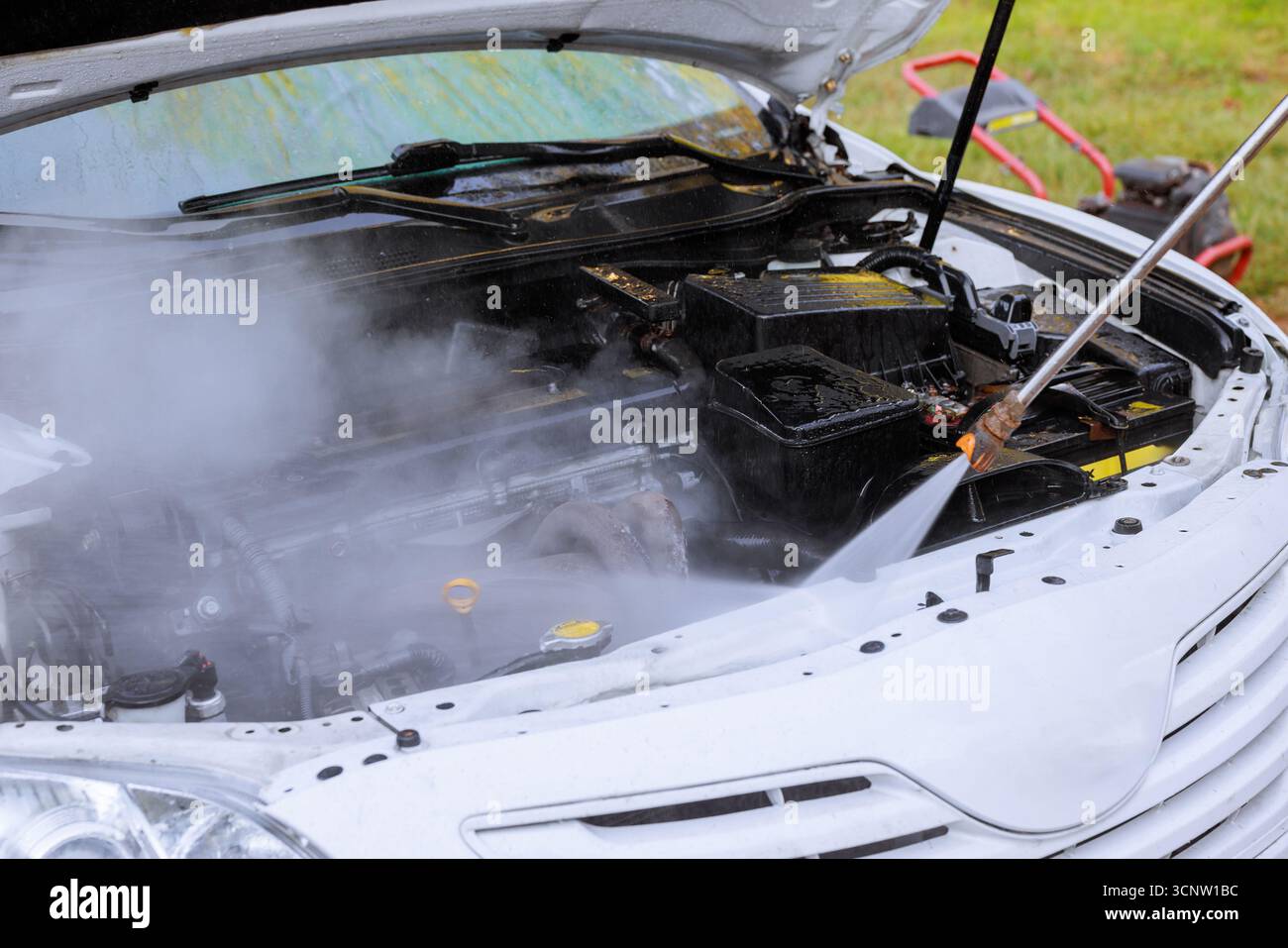 Il personale addetto alla manutenzione pulisce il motore dell'auto con un'idropulitrice che produce vapore Foto Stock