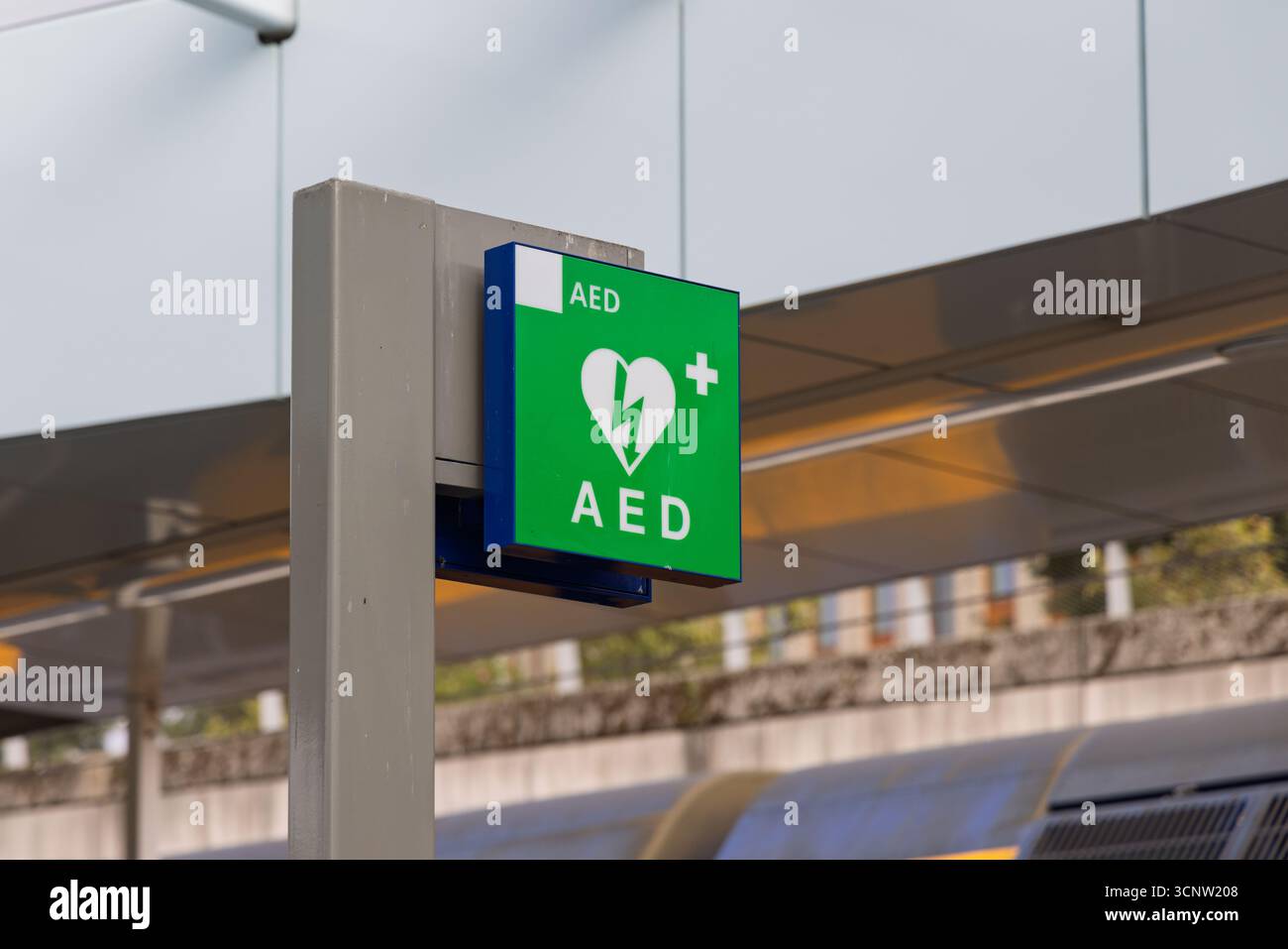 Cartello verde AED in una stazione ferroviaria moderna nei Paesi Bassi. Simbolo del defibrillatore pubblico per l'accesso alla rianimazione cardiaca di emergenza. Foto Stock