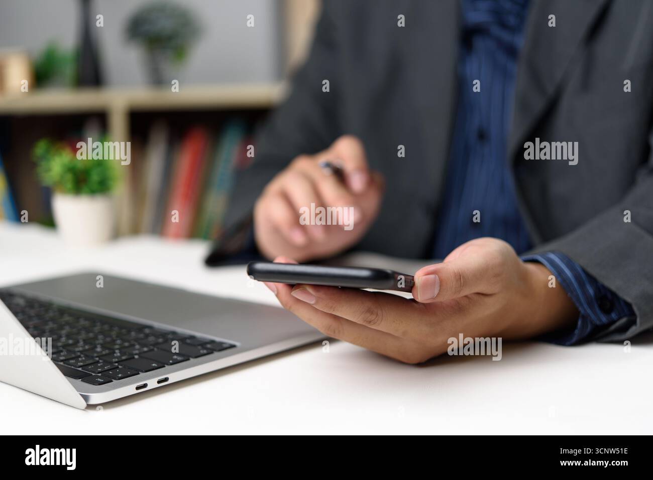 Uomo d'affari che utilizza smartphone e laptop in un ufficio moderno, rappresentando il flusso di lavoro digitale e la produttività mobile. Configurazione intelligente dell'ufficio per il lavoro in remoto Foto Stock