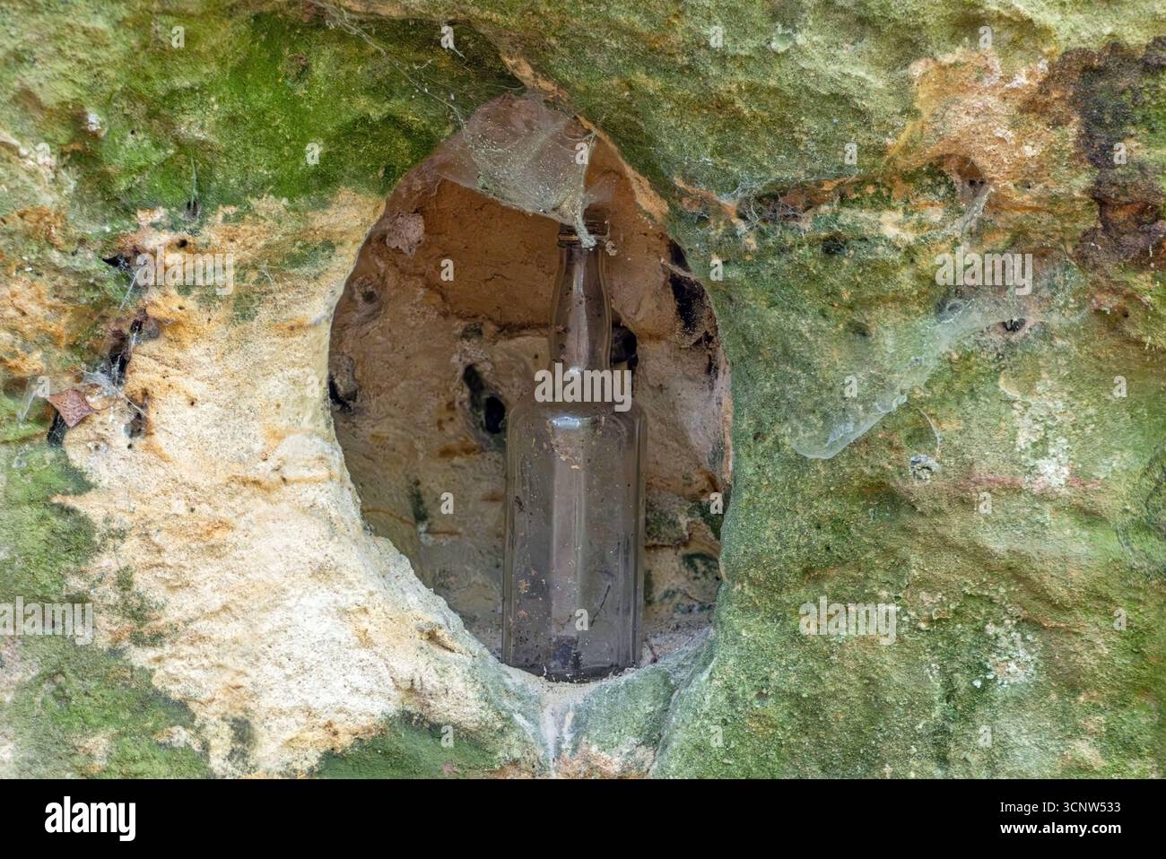 Vecchia bottiglia di vetro collocata in un piccolo foro intagliato in una parete rocciosa Foto Stock