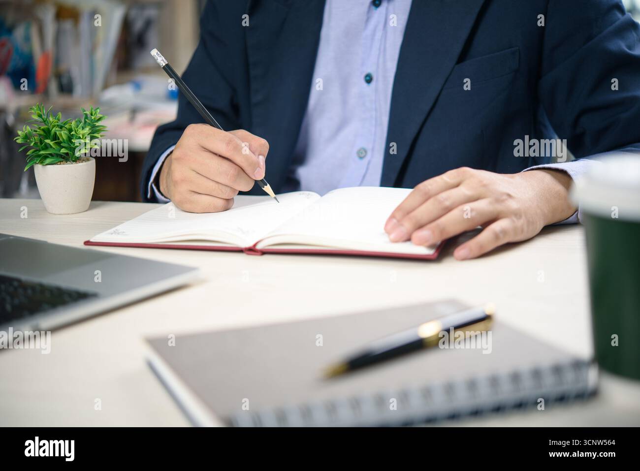 I dipendenti aziendali scrivono gli obiettivi in un notebook personale, lavorano a una scrivania organizzata con un impianto ecologico. Produttività, strategia e concetto di concentrazione per professare Foto Stock