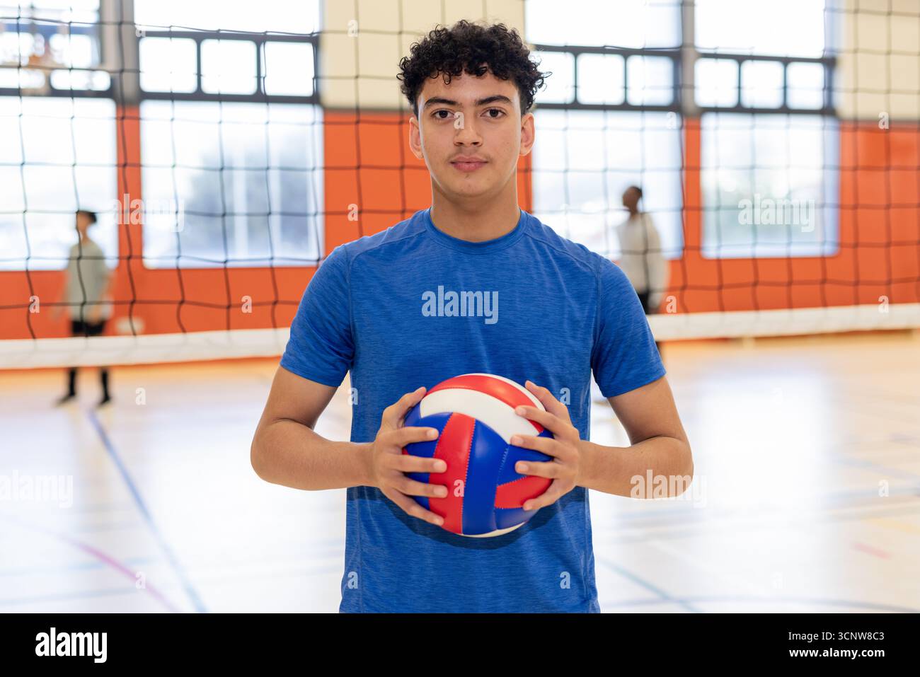 Compagni di squadra maschile di pallavolo in piedi in palestra a rete con il livello del petto rosso-bianco-blu Foto Stock