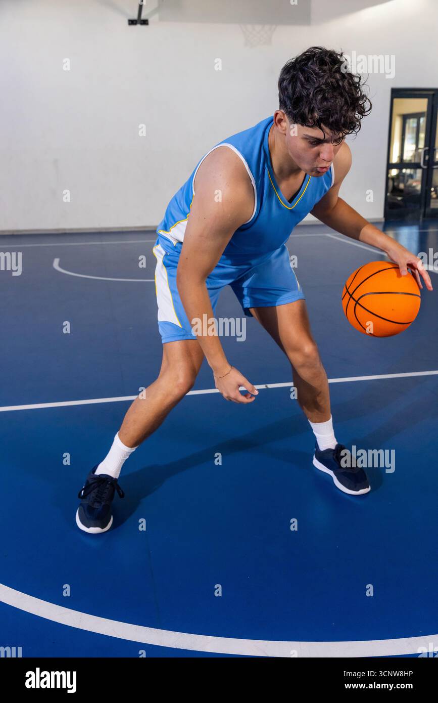 Atleta adolescente che pratica pallacanestro arancione sul campo in palestra vicino al cerchio e alla porta con pannello di vetro Foto Stock