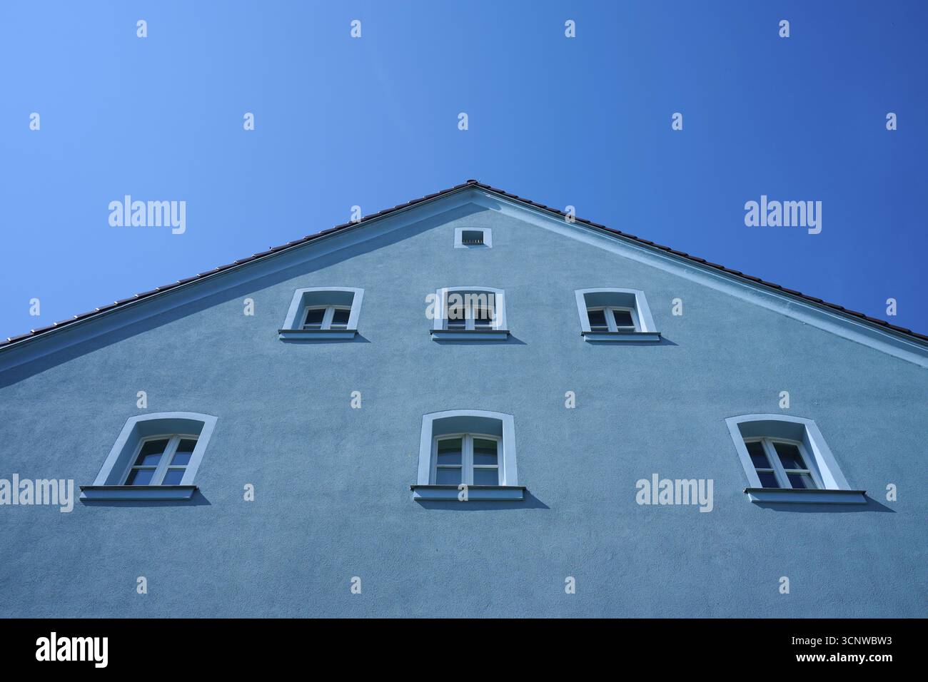 Casa blu con diverse finestre e tetto spiovente di fronte a un cielo blu brillante, Ratisbona, Baviera, Germania Foto Stock