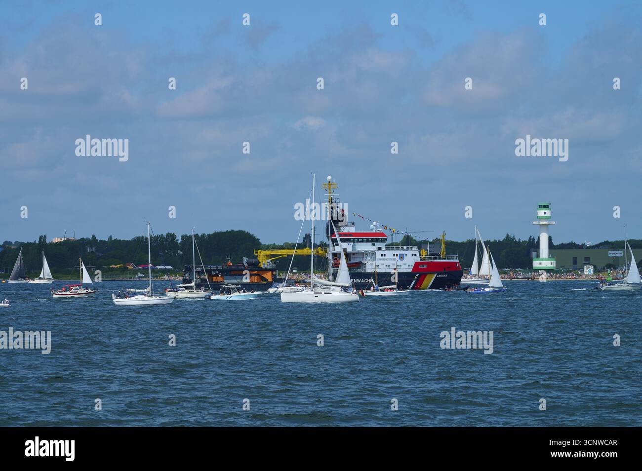 Grande nave della Guardia Costiera di Arkona e numerose piccole barche a vela in acqua di fronte a un faro Friedrichsort, Windjammer Parade Kiel 2025, dis Foto Stock
