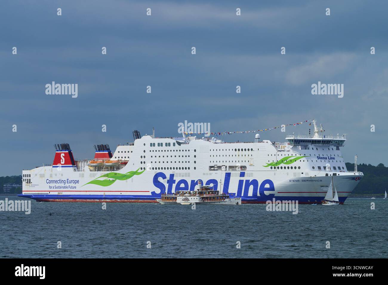 Grande traghetto della Stena Line sul mare, accompagnato da piccole barche a vela sotto un cielo nuvoloso, Windjammer Parade Kiel 2025, Heikendorf, distretto di Ploen, K. Foto Stock