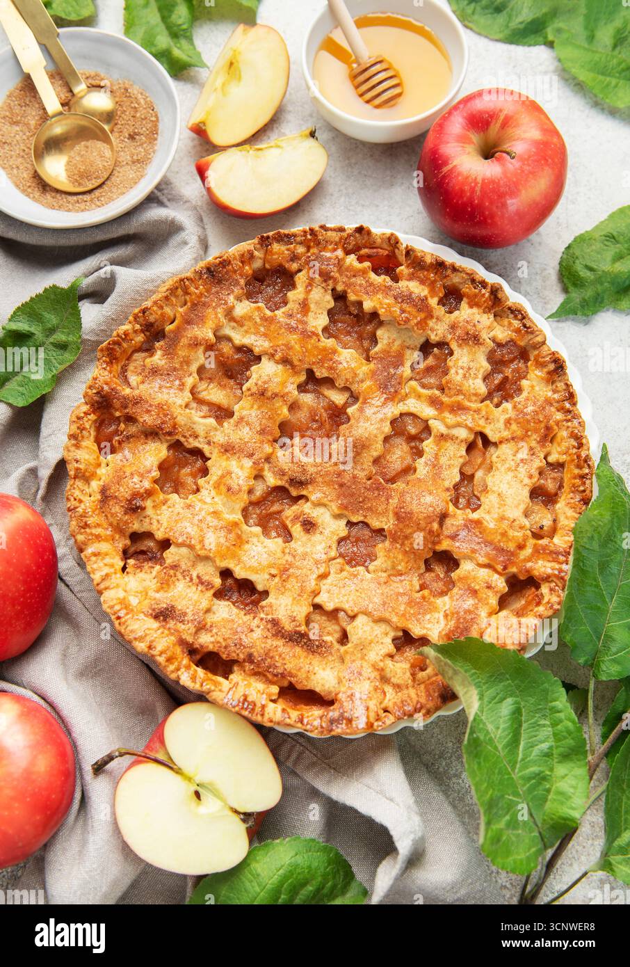 Classica torta di mele circondata da mele fresche, miele, zucchero di canna e decorata con foglie di mele Foto Stock