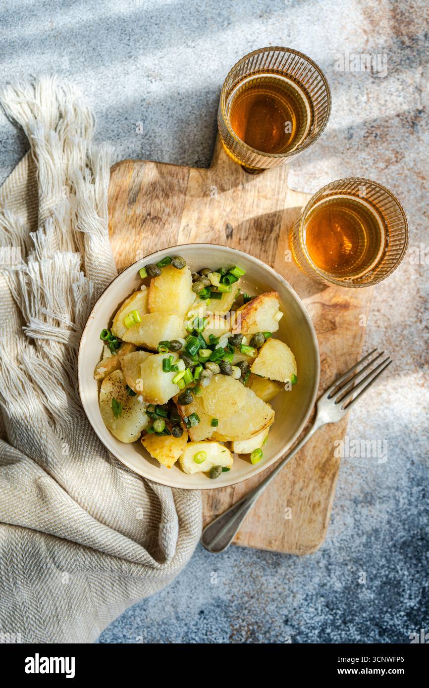 Vista dall'alto di una vivace insalata di patate greche in una ciotola, guarnita con capperi freschi ed erbe aromatiche, adagiata su una tavola rustica di legno, che crea un delizioso Mediter Foto Stock