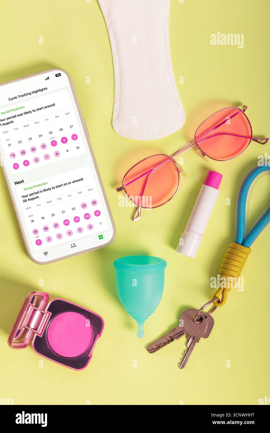 Uno smartphone moderno visualizza un'app di monitoraggio del periodo circondata da prodotti femminili essenziali come una tazza mestruale, un pad, occhiali da sole, rossetto e blu Foto Stock