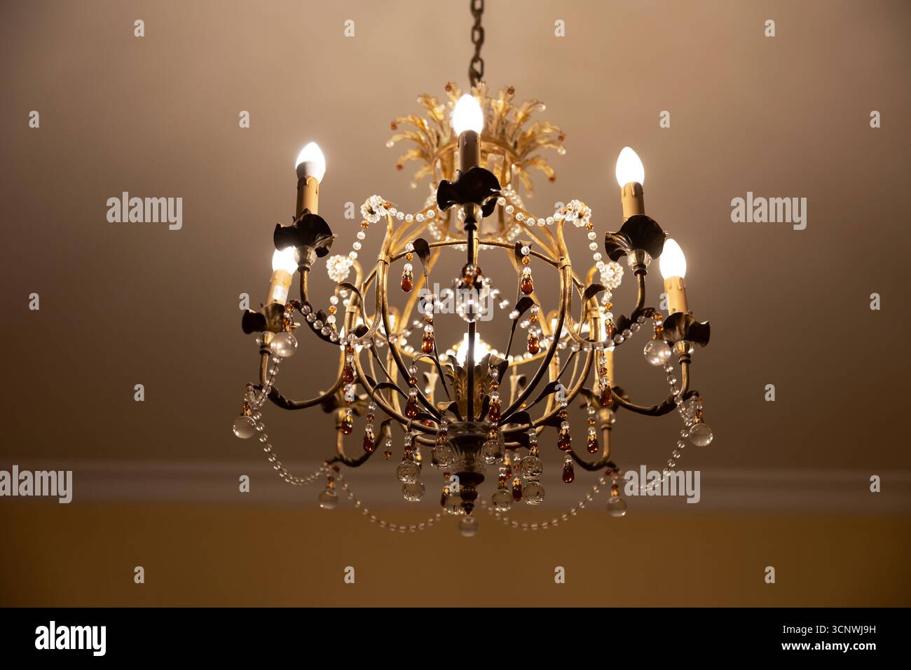 Un classico lampadario antico adornato da cristalli e delicati lavori in metallo. Il lampadario emana una luce soffusa e calda, aggiungendo eleganza e raffinatezza Foto Stock