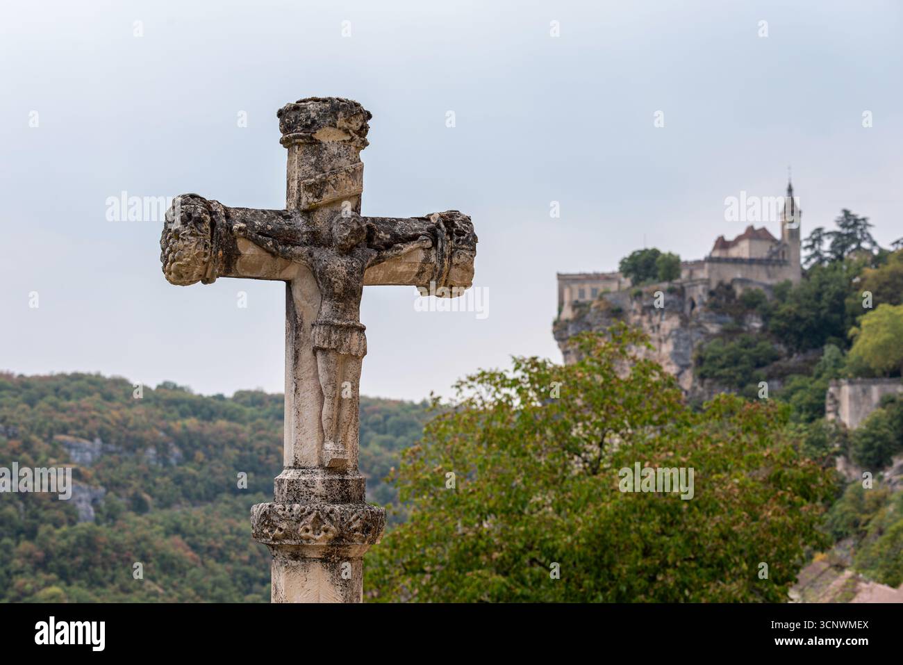 Bellissima antica croce medievale a lato strada in pietra con sullo sfondo il paesino panoramico di Rocamadour. Foto Stock