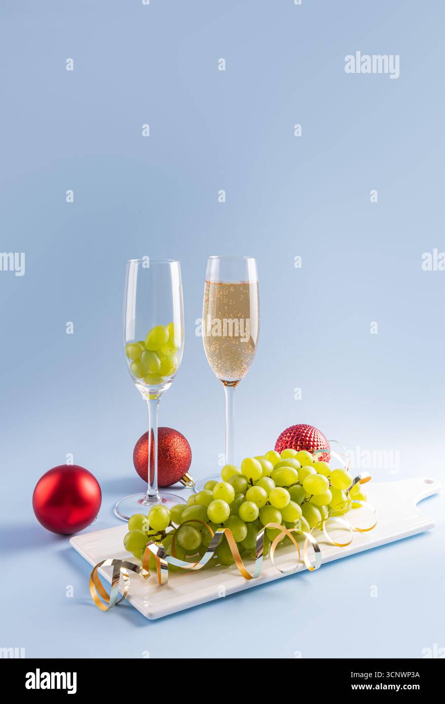 Celebra la tradizione spagnola di mangiare dodici uve, simboleggiando la fortuna per ogni mese, con un bicchiere di champagne la vigilia di Capodanno. Baubles festivi Foto Stock