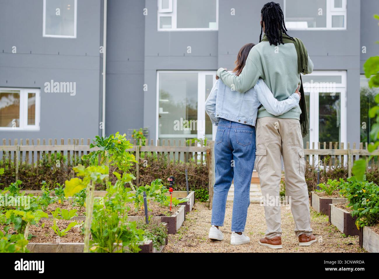 Diverse coppie che sorvegliano la casa cittadina attraverso il giardino della comunità con un percorso in trucioli di legno e letti rialzati Foto Stock