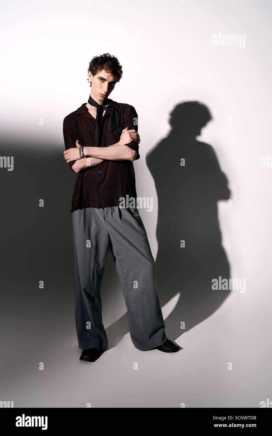 Un giovane elegante posa con fiducia, creando un'ombra audace su uno sfondo semplice. Foto Stock