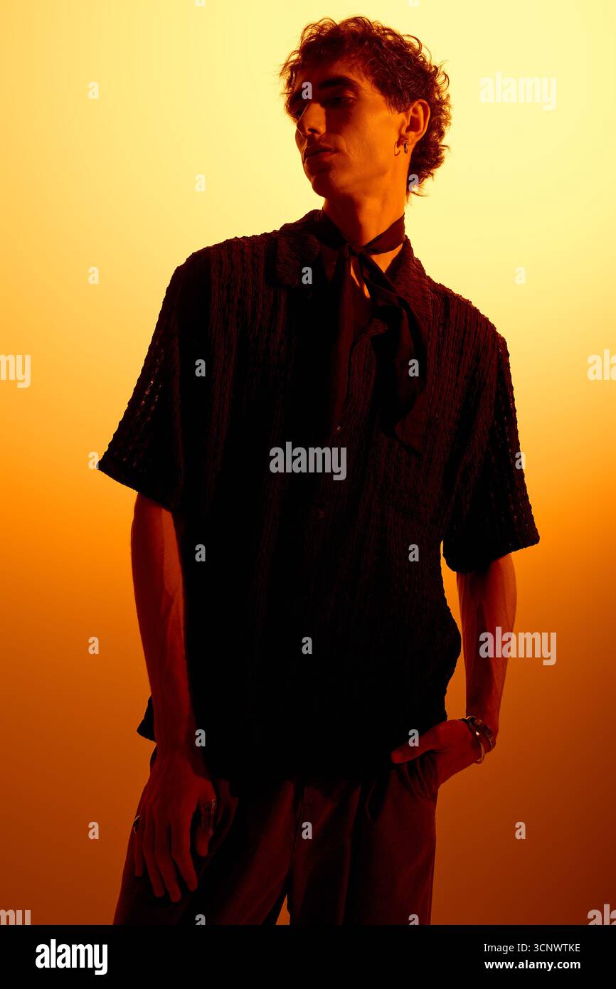 Un giovane uomo sicuro di sé si staglia in un abbigliamento alla moda, abbracciando il vibrante bagliore del tramonto. Foto Stock
