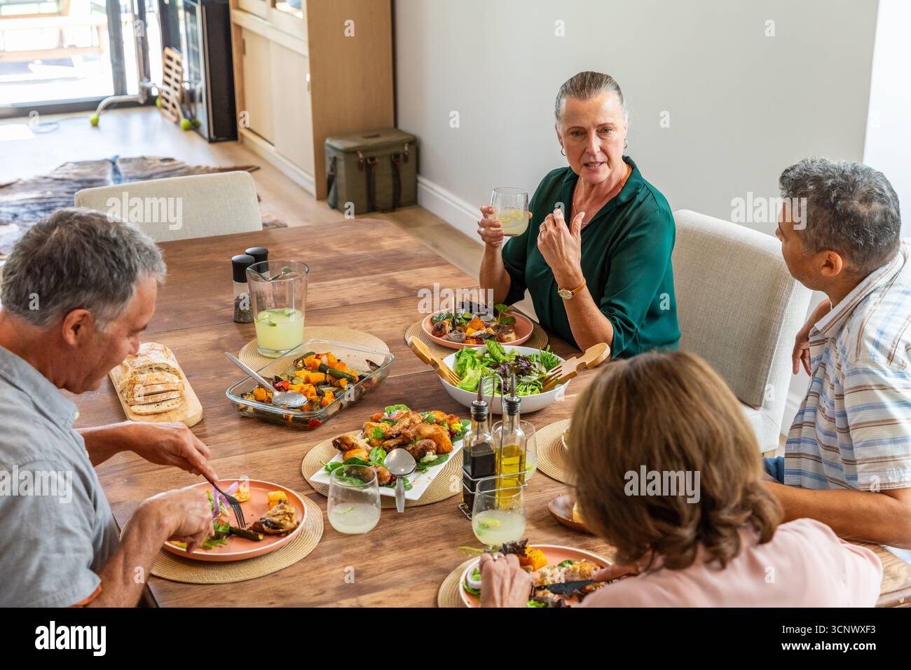 Diversi amici anziani che condividono il pasto a mezzogiorno al tavolo da pranzo a casa con insalata e limonata Foto Stock