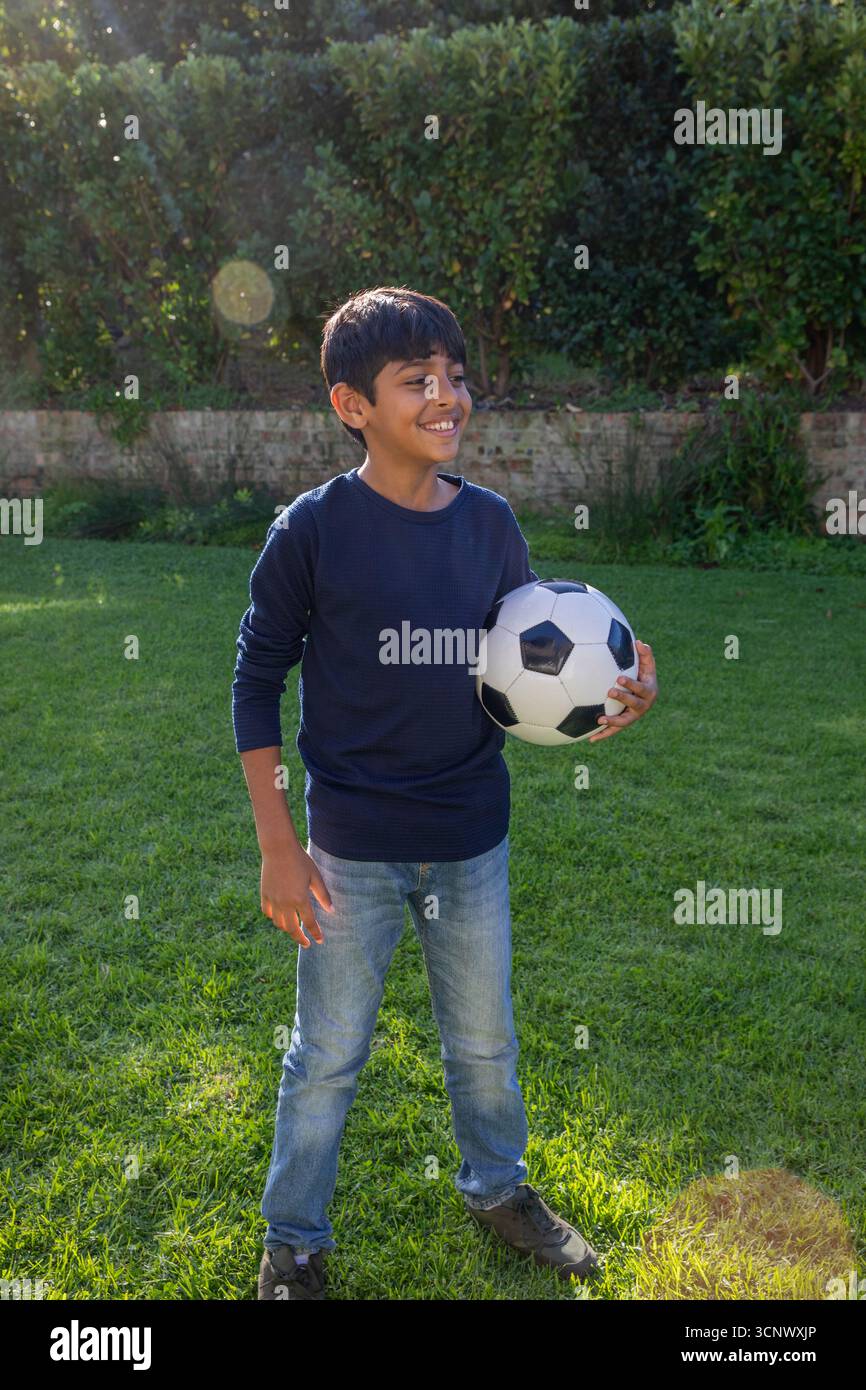 Ragazzo dell'asia meridionale in piedi sul prato in cortile con palla da calcio in bianco e nero Foto Stock