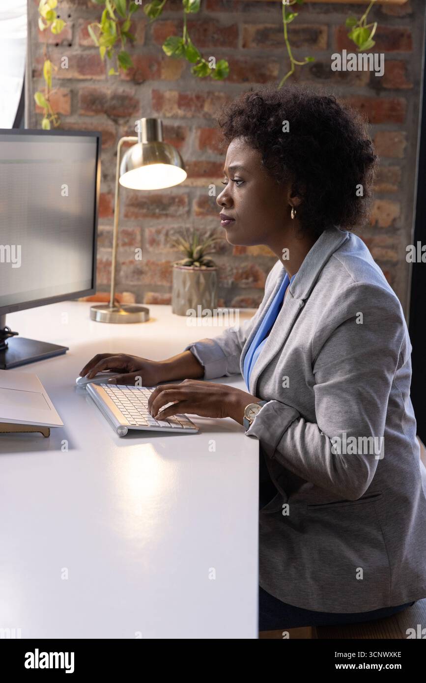 Donna afroamericana che scrive sulla tastiera alla scrivania dell'ufficio con blazer grigio, spazio copia Foto Stock