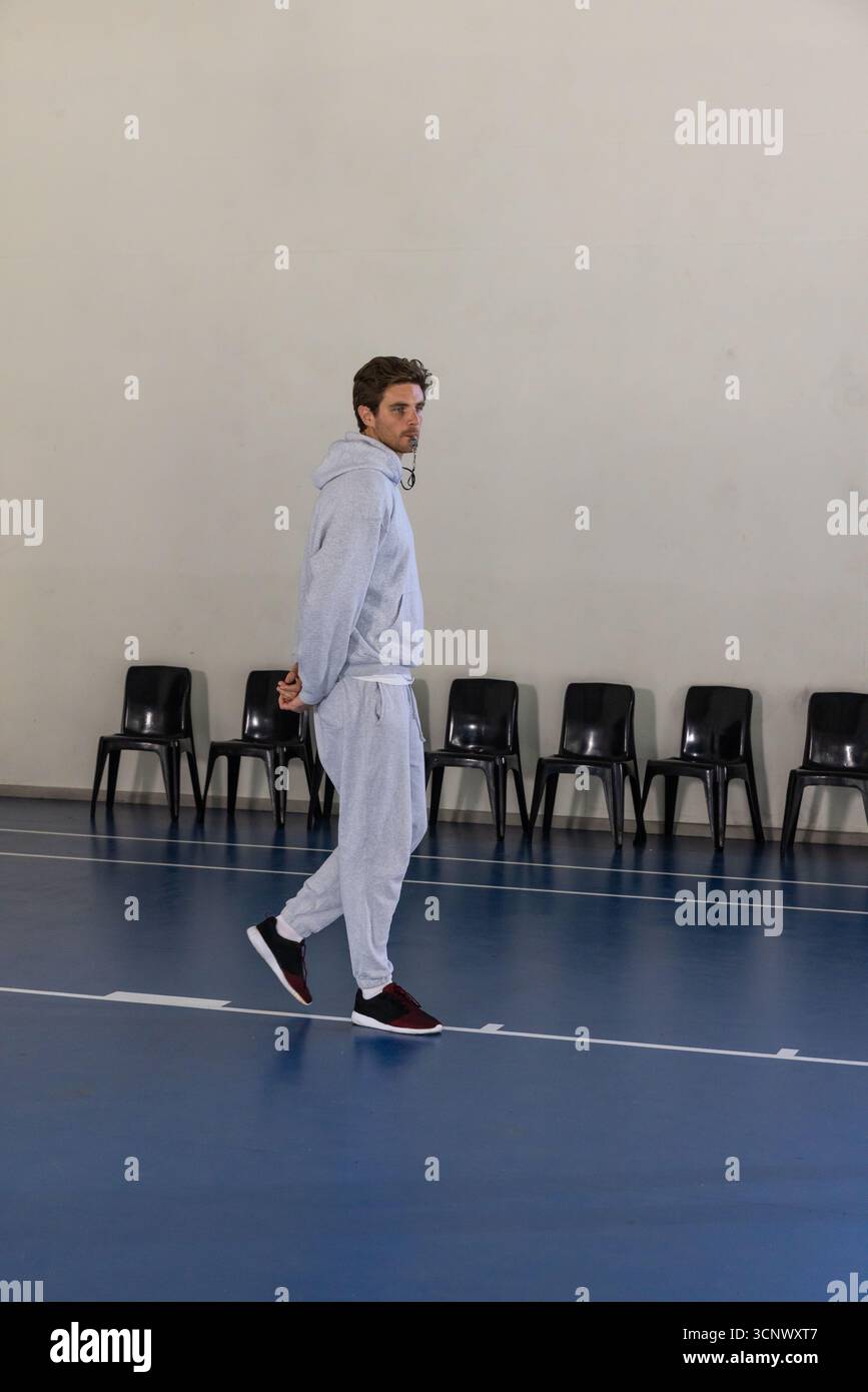 Uomo di 20 anni che cammina su un elegante campo da palestra blu con tuta e scarpe grigie Foto Stock