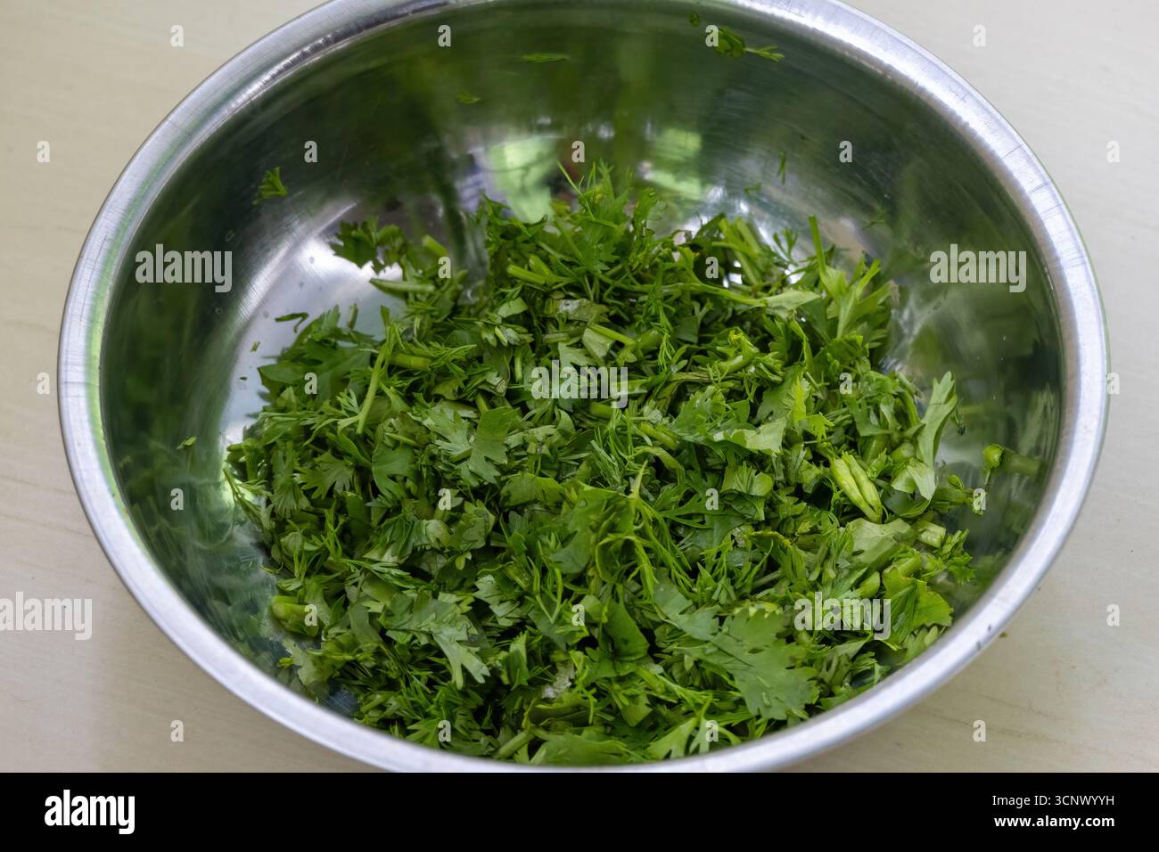 Foglie di coriandolo fresche in una ciotola di acciaio su fondo di legno. Il coriandolo è un altro nome per le foglie della pianta del coriandolo, Coriandrum sativum. Lo è Foto Stock