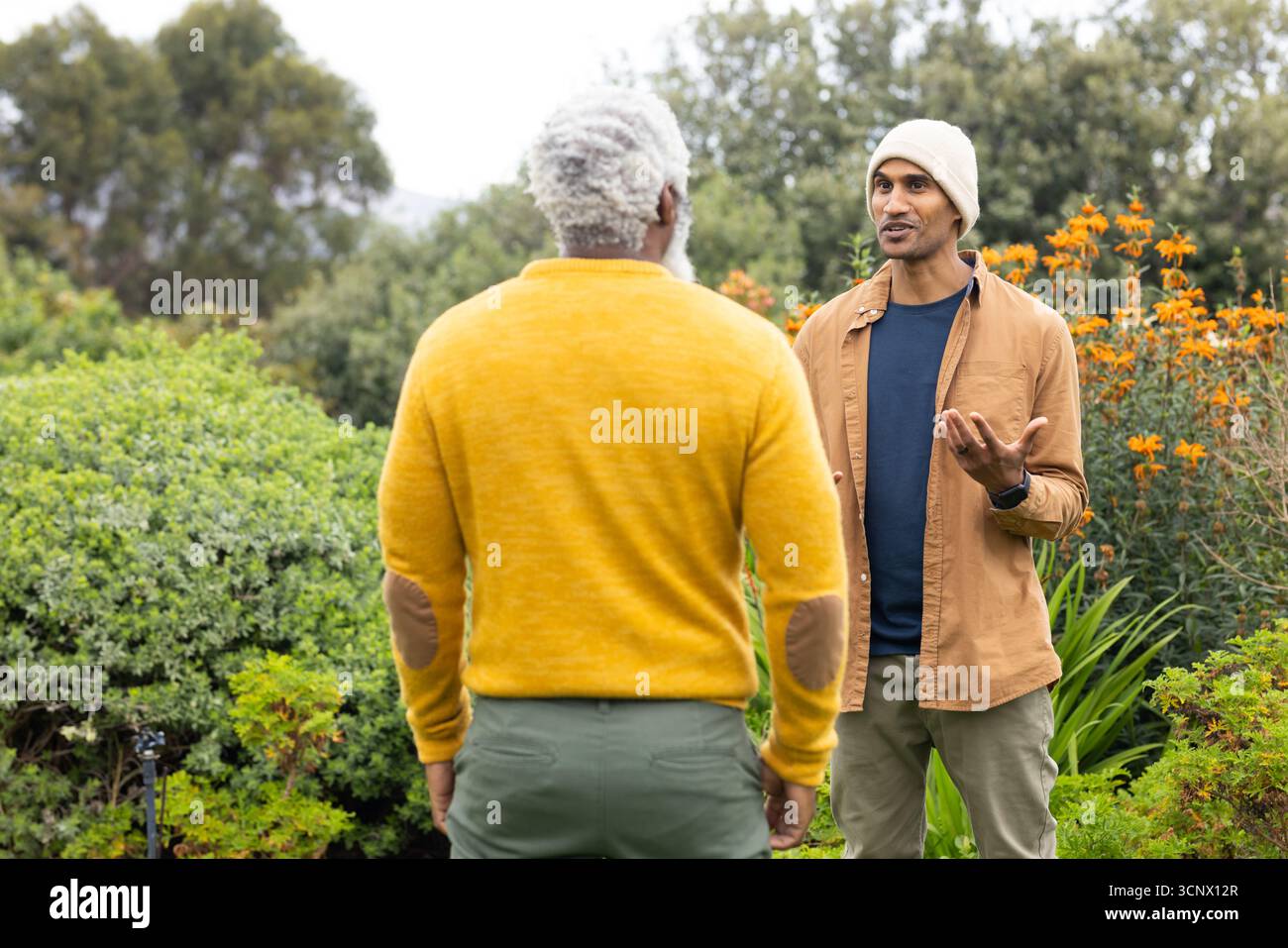 Diversi amici maschi chiacchierano mentre gestivano con lo smartwatch nel giardino residenziale del cortile Foto Stock