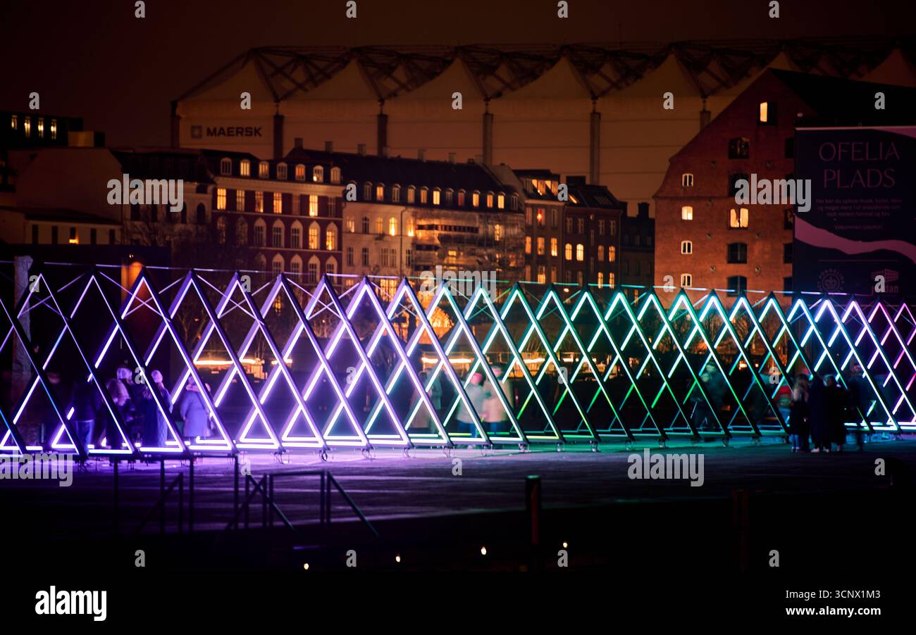 Ofelia Plads di notte: Un'installazione luminosa triangolare brilla contro edifici illuminati con l'edificio Maersk sul lungomare. Copenaghen Foto Stock