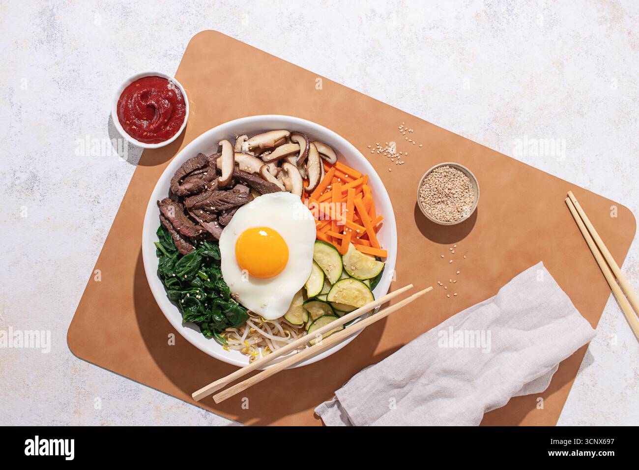 Foto sopra la testa di un bibimbap colorato ed equilibrato sotto la luce dura, con bacchette e semi di sesamo per un look minimalista Foto Stock