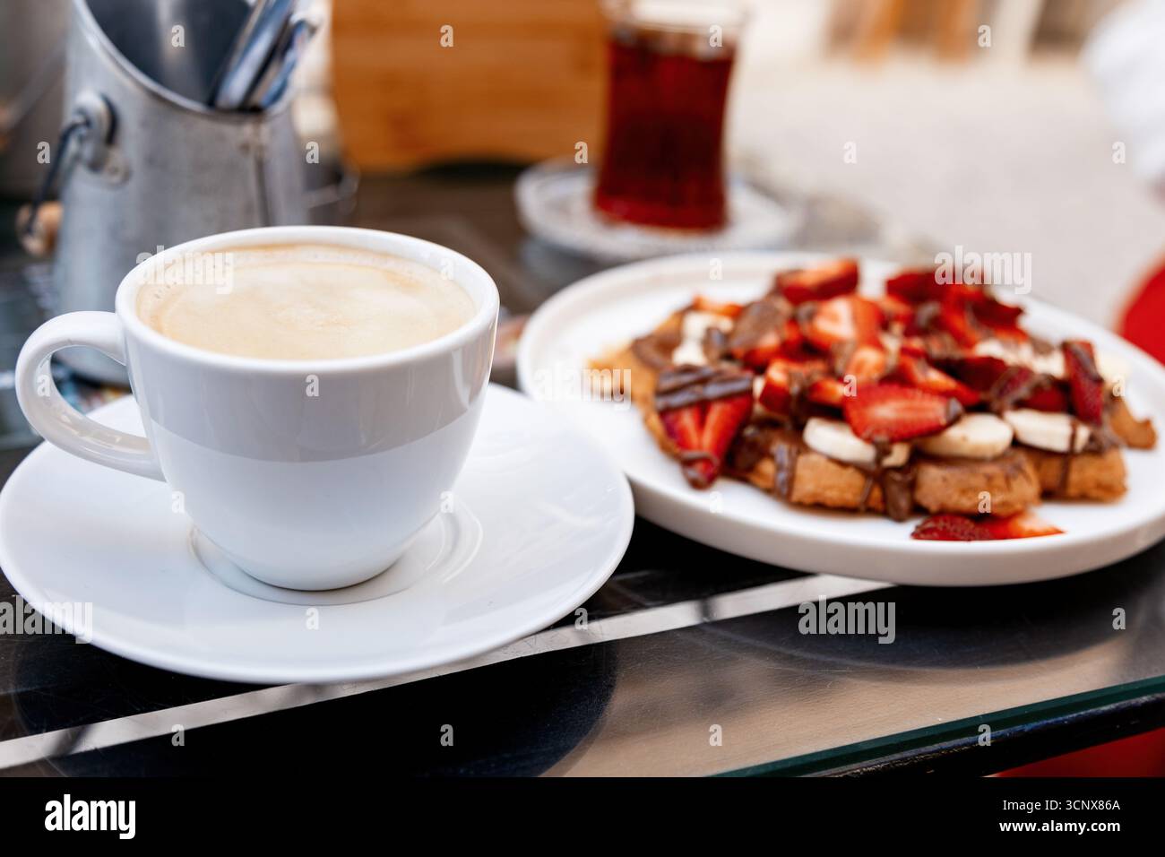 Una tazza di caffè fumante abbinata a deliziosi waffle conditi con fragole fresche e salsa al cioccolato, serviti su un tavolo in un'accogliente atmosfera da caffè Foto Stock