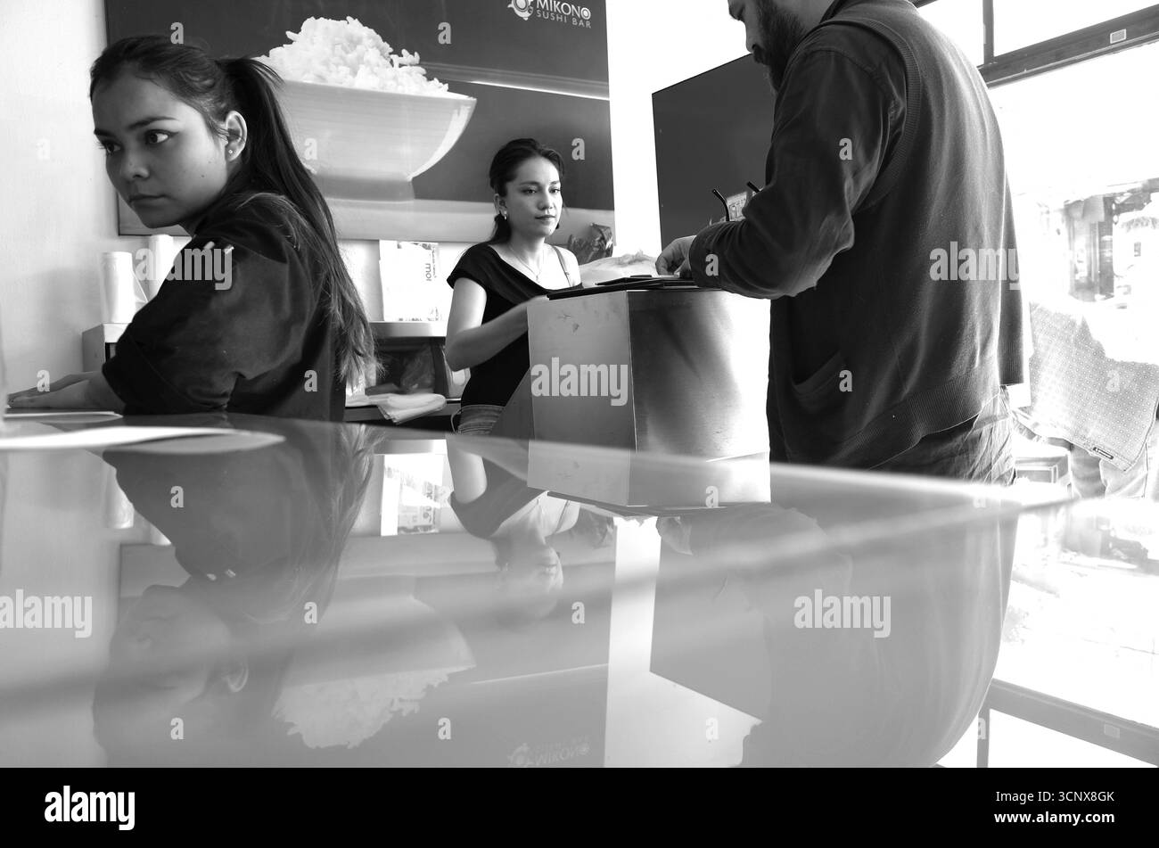 Il personale del ristorante e i clienti interagiscono presso un bancone informale di cibo messicano-giapponese Foto Stock
