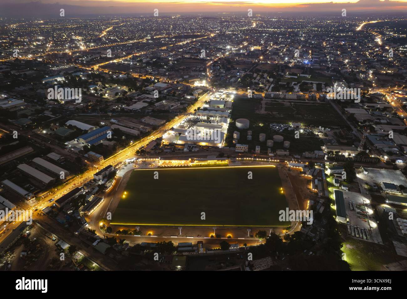 Veduta aerea di uno stadio illuminato vicino a Club Road, il suo vibrante campo verde che contrasta con il paesaggio urbano circostante sotto il cielo crepuscolo, Kano, Kano, Nigeria. Foto Stock